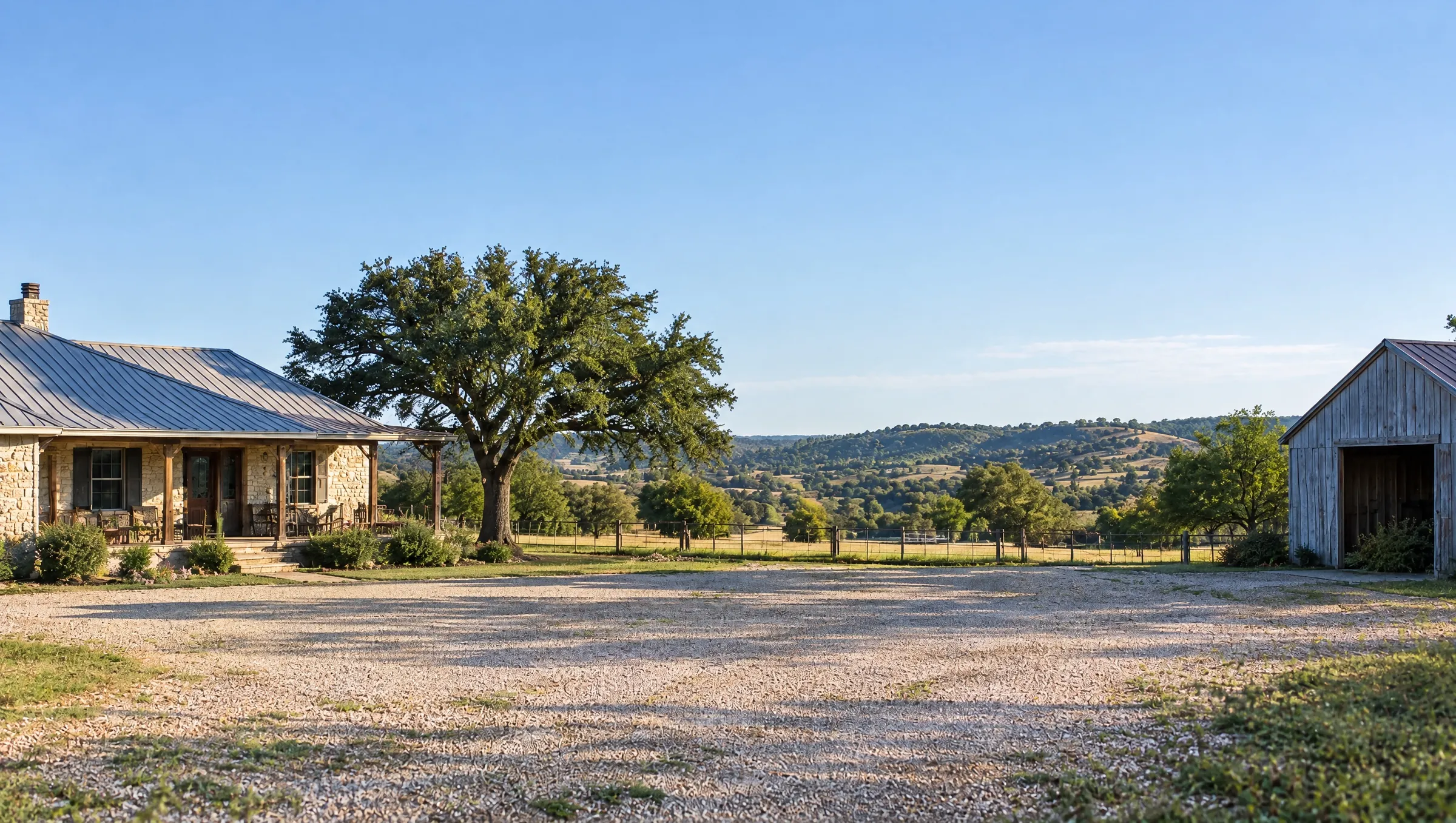 A Texas home beside an oak tree, with hills and a barn beyond the driveway